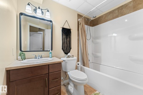 The bathroom features a vanity with a white basin sink, a wall-mounted rectangular mirror, and a shower-tub combination with tiled walls - 112 Lakeland Point(E), Beaumont, AB - Indoor Photo Showing Bathroom