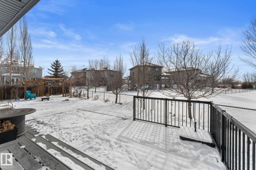 The property features an outdoor deck with black metal railings, overlooking a snow-covered yard with a wooden pergola structure - 112 Lakeland Point(E), Beaumont, AB - Outdoor