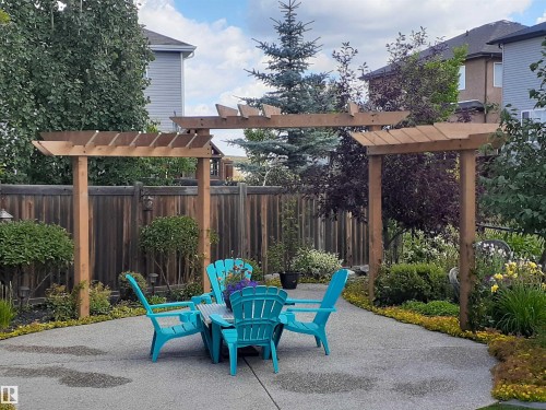 The property features a private outdoor patio area with a wooden pergola, surrounded by mature trees and landscaped garden beds - 112 Lakeland Point(E), Beaumont, AB - Outdoor