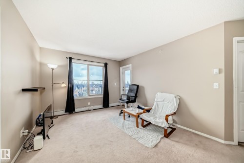 Spacious living area featuring neutral-toned carpeting, a large multi-pane window, and a white paneled door leading to an exterior space - 404 12025 22 Avenue Sw, Edmonton, AB - Indoor