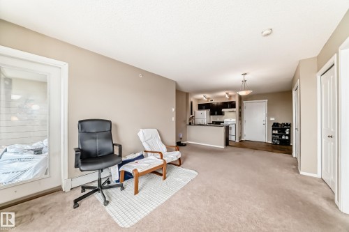 Open-concept living space featuring neutral carpet, a kitchen with dark cabinetry, and an island with a breakfast bar - 404 12025 22 Avenue Sw, Edmonton, AB - Indoor