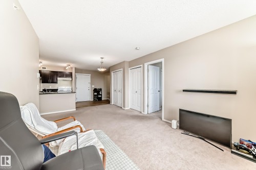 Open-concept living space with neutral paint, carpet flooring, a built-in wall shelf, and two interior doors - 404 12025 22 Avenue Sw, Edmonton, AB - Indoor