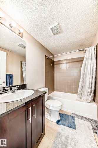 Bathroom featuring a dark wood-finish vanity with a built-in sink, stone-finish countertop, and wall-mounted mirror - 404 12025 22 Avenue Sw, Edmonton, AB - Indoor Photo Showing Bathroom
