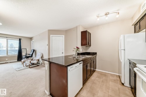 Building entrance featuring a covered portico with recessed lighting, dual glass entry doors, and a stone accent facade - 404 12025 22 Avenue Sw, Edmonton, AB - Outdoor With Balcony With Exterior