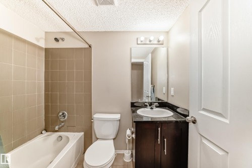 Bathroom featuring a white tub, beige wall tiling, dark wood-finish vanity with a dark countertop, and a mirrored vanity light fixture - 404 12025 22 Avenue Sw, Edmonton, AB - Indoor Photo Showing Bathroom