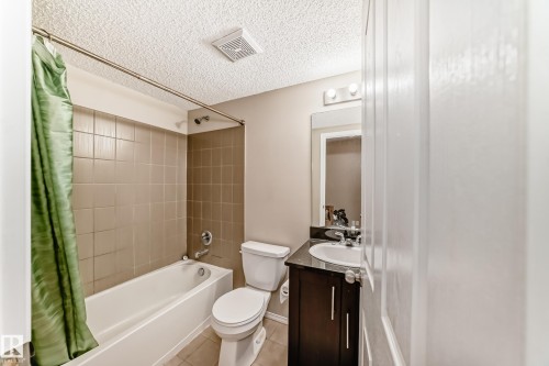 Bathroom featuring a white bathtub, beige wall tiling, and a dark wood-finish vanity with a white sink and dark countertop - 404 12025 22 Avenue Sw, Edmonton, AB - Indoor Photo Showing Bathroom