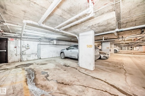 Designated parking space within a subterranean garage, featuring concrete flooring, exposed overhead piping, and fluorescent lighting - 404 12025 22 Avenue Sw, Edmonton, AB - Indoor Photo Showing Garage