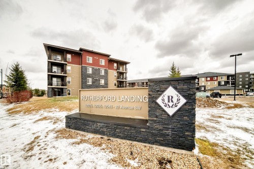 Entry monument featuring stacked stone, a custom emblem, and property identification - 404 12025 22 Avenue Sw, Edmonton, AB - Outdoor