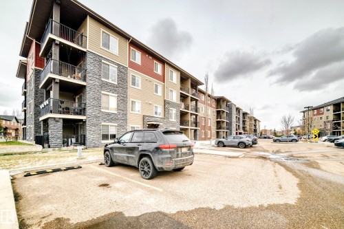 Multi-story building featuring stone and siding exterior accents, private balconies, and an adjacent asphalt parking area - 404 12025 22 Avenue Sw, Edmonton, AB - Outdoor With Balcony