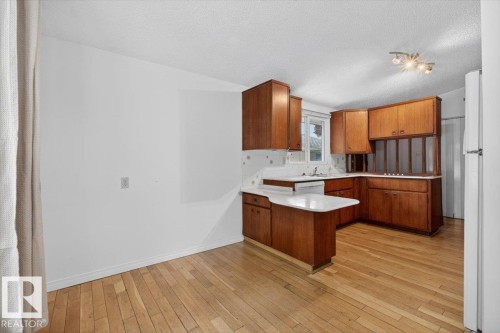 Kitchen featuring wood cabinetry, white countertops, built-in dishwasher, and wood-finish flooring - 6018 105A Street, Edmonton, AB 