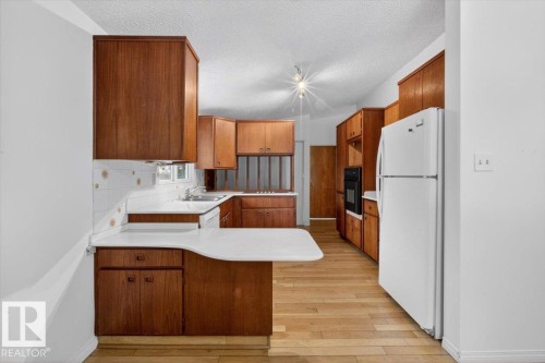 Kitchen featuring extensive wood cabinetry, white countertops, a built-in oven, and wood-finish flooring - 6018 105A Street, Edmonton, AB 