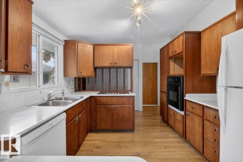 Kitchen featuring wood-finish cabinetry, a double basin stainless steel sink, built-in oven, and wood-finish flooring - 6018 105A Street, Edmonton, AB 