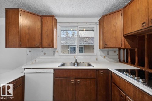 Kitchen featuring wood cabinetry, white countertops, a double basin stainless steel sink, and a built-in electric cooktop - 6018 105A Street, Edmonton, AB 