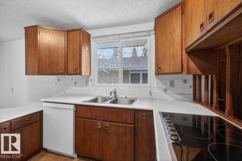 Kitchen featuring wood-finish cabinetry, a double basin stainless steel sink, a built-in dishwasher, white countertops, and a black electric cooktop - 6018 105A Street, Edmonton, AB 