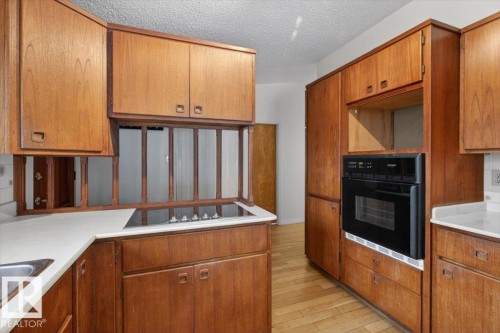 Kitchen featuring wood cabinetry, light countertops, a built-in oven, and a cooktop - 6018 105A Street, Edmonton, AB 
