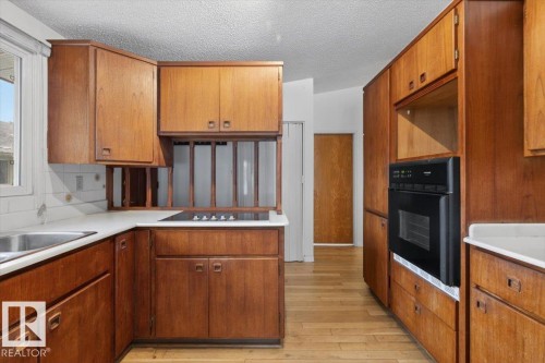 Kitchen featuring wood cabinetry, white countertops, a built-in oven, and a cooktop - 6018 105A Street, Edmonton, AB 