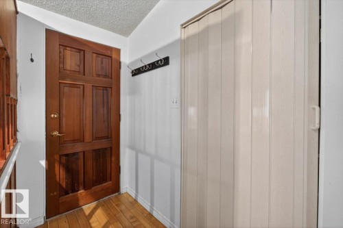 Paneled wood door with brass hardware, wood-finish flooring, and a folding closet door - 6018 105A Street, Edmonton, AB 