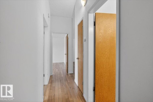 Corridor featuring wood-finish flooring, white walls, and multiple light wood interior doors with silver-tone hardware - 6018 105A Street, Edmonton, AB 