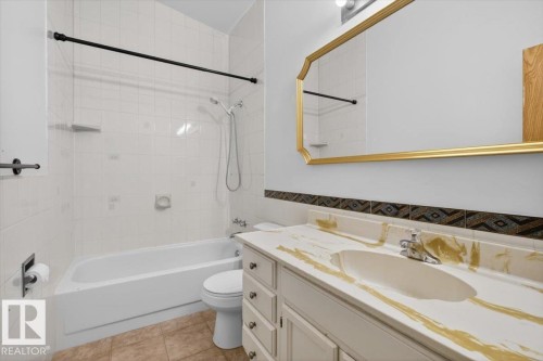 Bathroom featuring a white bathtub with subway tile surround, a vanity with a patterned countertop, and a decorative gold-framed mirror - 6018 105A Street, Edmonton, AB 