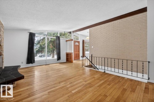 Expansive living area featuring wood-finish flooring, a stone fireplace, and a light brick accent wall - 6018 105A Street, Edmonton, AB 