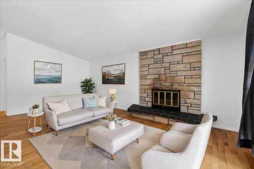 Living area featuring a stone accent wall with an integrated fireplace, wood-finish flooring, and white painted walls - 6018 105A Street, Edmonton, AB 