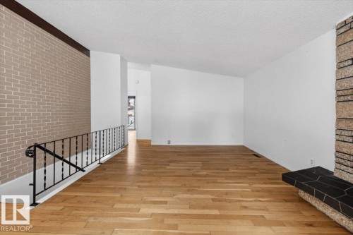 Spacious interior featuring wood-finish flooring, a stone-clad fireplace with a dark tile hearth, and a brick accent wall with a dark wood trim - 6018 105A Street, Edmonton, AB 