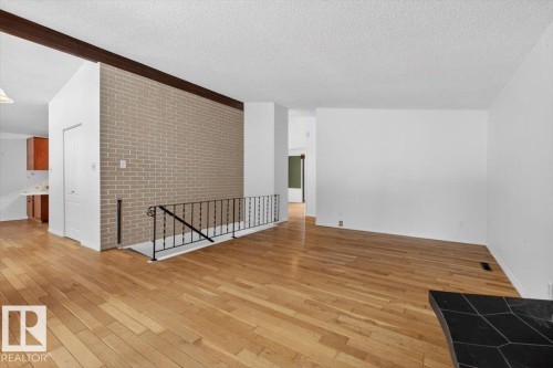 Open living space featuring wood-finish flooring, a light-colored brick accent wall, and a black metal handrail - 6018 105A Street, Edmonton, AB 