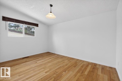 Room featuring wood flooring, white painted walls, a window with a dark wood-finish blind, and a ceiling-mounted pendant light fixture - 6018 105A Street, Edmonton, AB 
