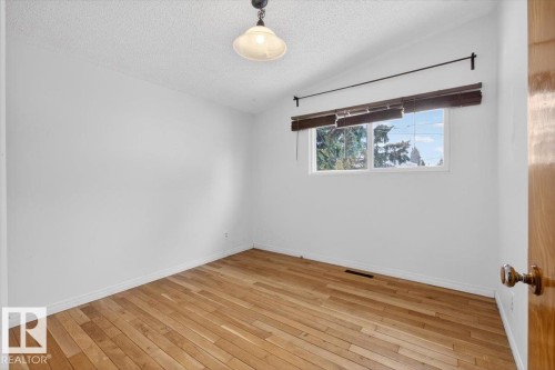 Light-filled room featuring wood-finish flooring, white baseboards, and a single window with blinds - 6018 105A Street, Edmonton, AB 