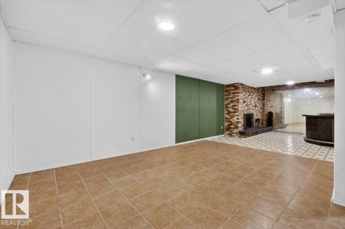 Spacious lower-level area featuring a brick fireplace, built-in bar, and two distinct tile flooring patterns - 6018 105A Street, Edmonton, AB 