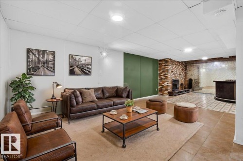 Spacious recreation room featuring a brick fireplace, drop ceiling with recessed lighting, and a built-in bar area - 6018 105A Street, Edmonton, AB 