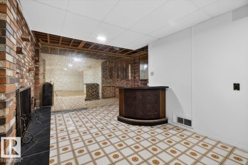 Tiled flooring with a decorative pattern throughout, featuring a brick fireplace with a black hearth and decorative screen - 6018 105A Street, Edmonton, AB 
