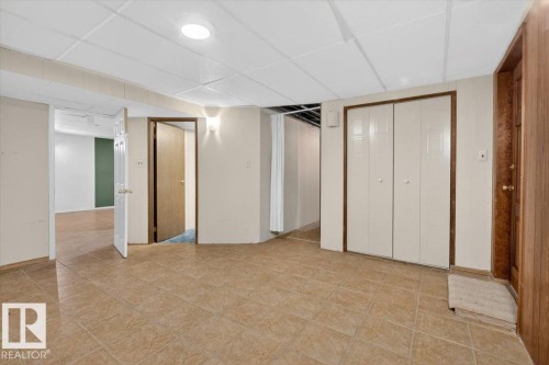 Spacious room featuring neutral-toned tile flooring, drop ceiling, recessed lighting, and access to additional rooms - 6018 105A Street, Edmonton, AB 