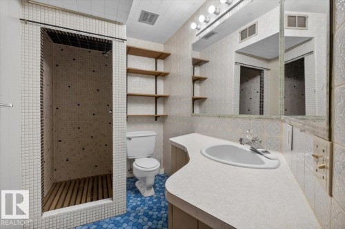 Bathroom featuring a standing shower with slatted wood flooring, mosaic tile walls, a vanity with an integrated sink, a wall-mounted mirror, and open shelving - 6018 105A Street, Edmonton, AB 