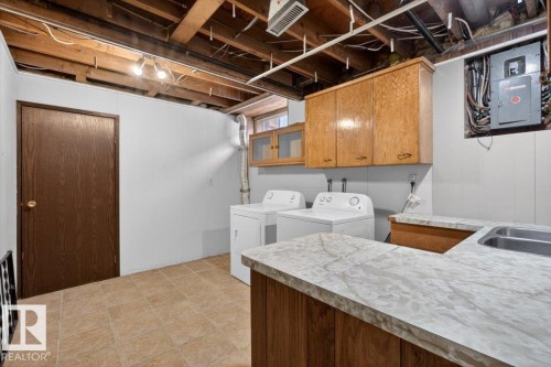 Functional laundry area featuring a double basin sink, light-toned countertop, and wood-finish cabinetry - 6018 105A Street, Edmonton, AB 