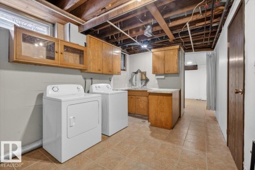Laundry area featuring wood-finish cabinetry, tile flooring, and a utility sink with a countertop - 6018 105A Street, Edmonton, AB 