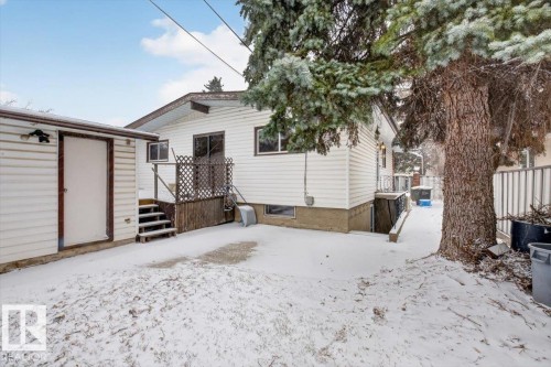 Rear exterior showcasing white horizontal siding, a private deck with lattice railing, a detached utility shed, and a mature tree - 6018 105A Street, Edmonton, AB 