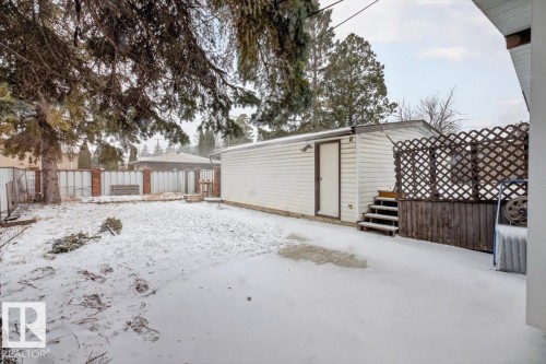 Spacious backyard featuring a detached garage with exterior siding, a multi-level deck with lattice privacy screening, mature evergreen trees, and a brick and metal fence - 6018 105A Street, Edmonton, AB 