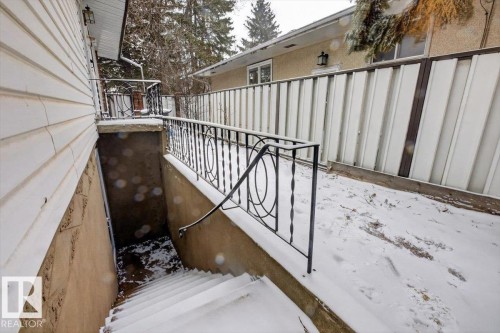 Exterior side entrance with a black wrought iron railing, concrete steps, and a stucco wall - 6018 105A Street, Edmonton, AB 