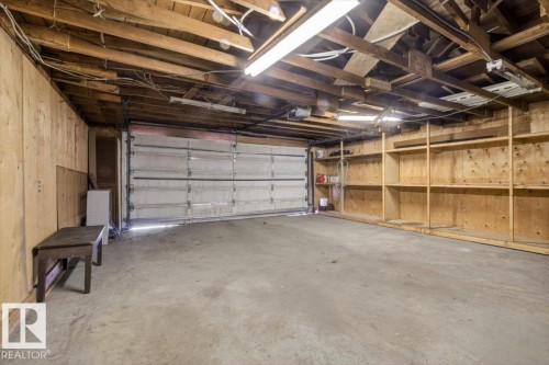 Spacious garage featuring a concrete floor, exposed wood beam ceiling, and a paneled garage door - 6018 105A Street, Edmonton, AB 