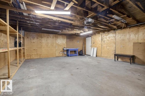 Spacious unfinished interior featuring exposed wood ceiling joists, concrete flooring, plywood walls, and built-in wood shelving units - 6018 105A Street, Edmonton, AB 