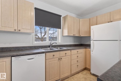 Kitchen featuring light wood-finish cabinetry, dark countertops, a double basin stainless steel sink, and a white refrigerator - 1904 36 Avenue, Edmonton, AB - Indoor Photo Showing Kitchen With Double Sink