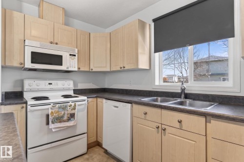 Kitchen featuring wood-finish cabinetry, built-in microwave, white electric range, white dishwasher, and a double basin stainless steel sink - 1904 36 Avenue, Edmonton, AB - Indoor Photo Showing Kitchen With Double Sink