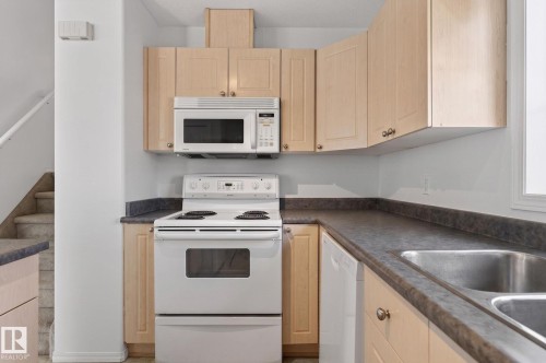 Functional kitchen featuring light wood-finish cabinetry, dark countertops, a white electric range, and an integrated double stainless steel sink - 1904 36 Avenue, Edmonton, AB - Indoor Photo Showing Kitchen