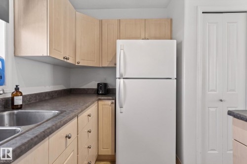 Kitchen space featuring a white top-freezer refrigerator, light wood-finish cabinetry with silver hardware, dark countertops, a double basin stainless steel sink, and a white bi-fold door - 1904 36 Avenue, Edmonton, AB - Indoor Photo Showing Kitchen With Double Sink