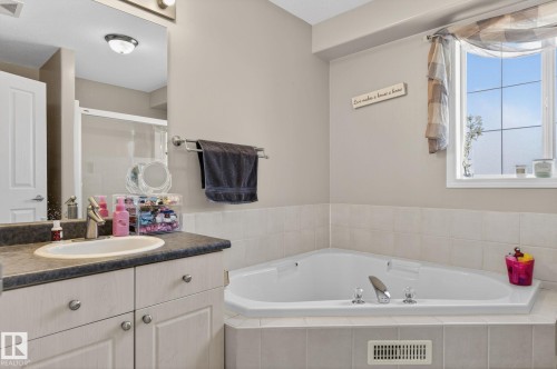 Corner soaking tub with tiled surround, light-colored vanity with a built-in sink, dark countertop, and a window providing natural illumination - 1904 36 Avenue, Edmonton, AB - Indoor Photo Showing Bathroom