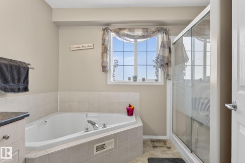 Bathroom featuring a corner soaking tub with tile surround, a separate glass-enclosed shower, a large window, a vanity with a dark countertop, and light-toned wall paint - 1904 36 Avenue, Edmonton, AB - Indoor Photo Showing Bathroom