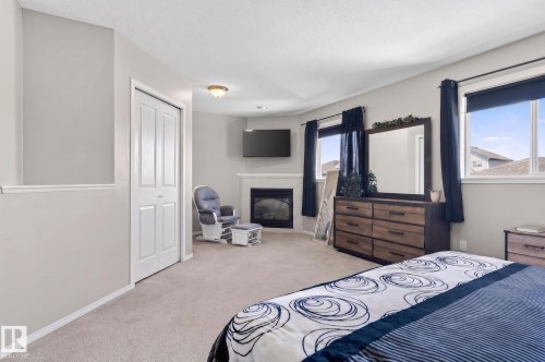 Carpeted room featuring a corner fireplace with a white mantel, two windows, a ceiling-mounted light fixture, and a bifold closet door - 1904 36 Avenue, Edmonton, AB - Indoor Photo Showing Bedroom