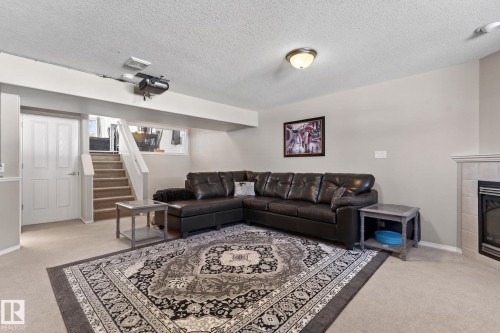 Finished lower level featuring a carpeted floor, recessed window, white paneled door, and a built-in fireplace with a tiled surround and mantel - 1904 36 Avenue, Edmonton, AB - Indoor Photo Showing Living Room With Fireplace