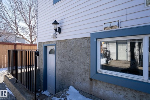 Lower-level entry featuring a white paneled door with an arched window, stucco foundation, and a black metal railing - 1904 36 Avenue, Edmonton, AB - Outdoor With Exterior